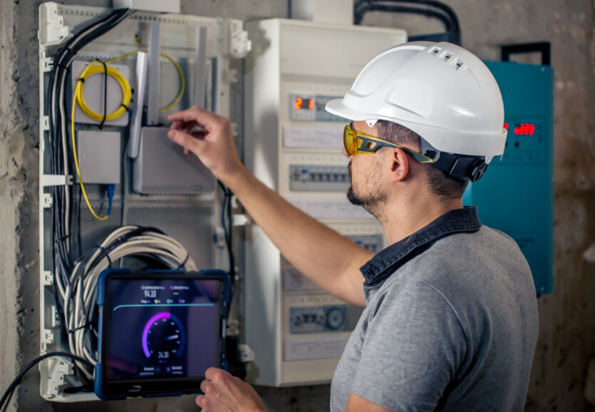 Man, an electrical technician working in a switchboard with fuses, uses a tablet.